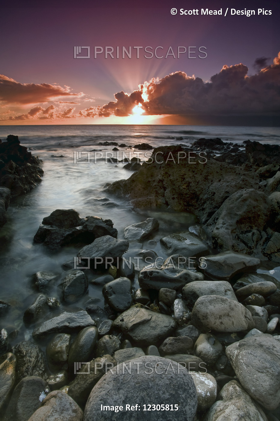 Sun Rays Shine Above The Clouds As The Sun Sets Over The Ocean With Rocks Along ...
