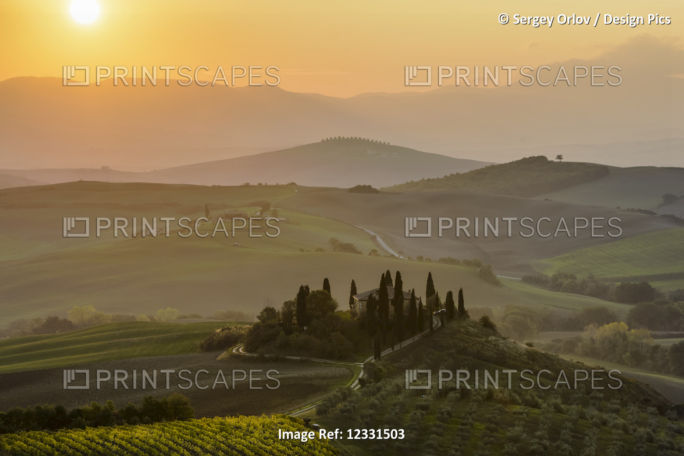 The morning sun rising above layered Tuscany green hills and the small Podere ...