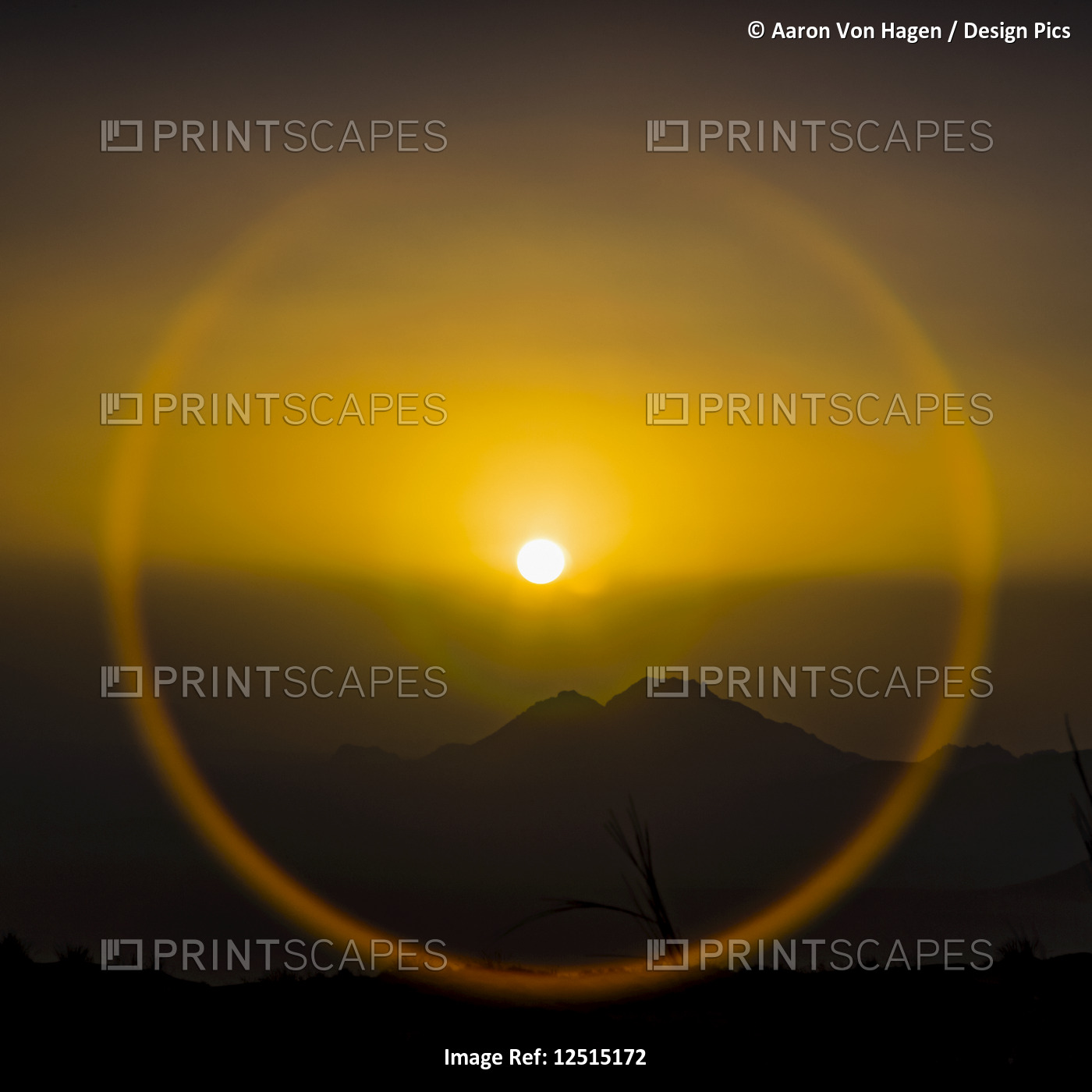 Halo around the glowing, golden sun over the silhouetted sand dunes of the ...