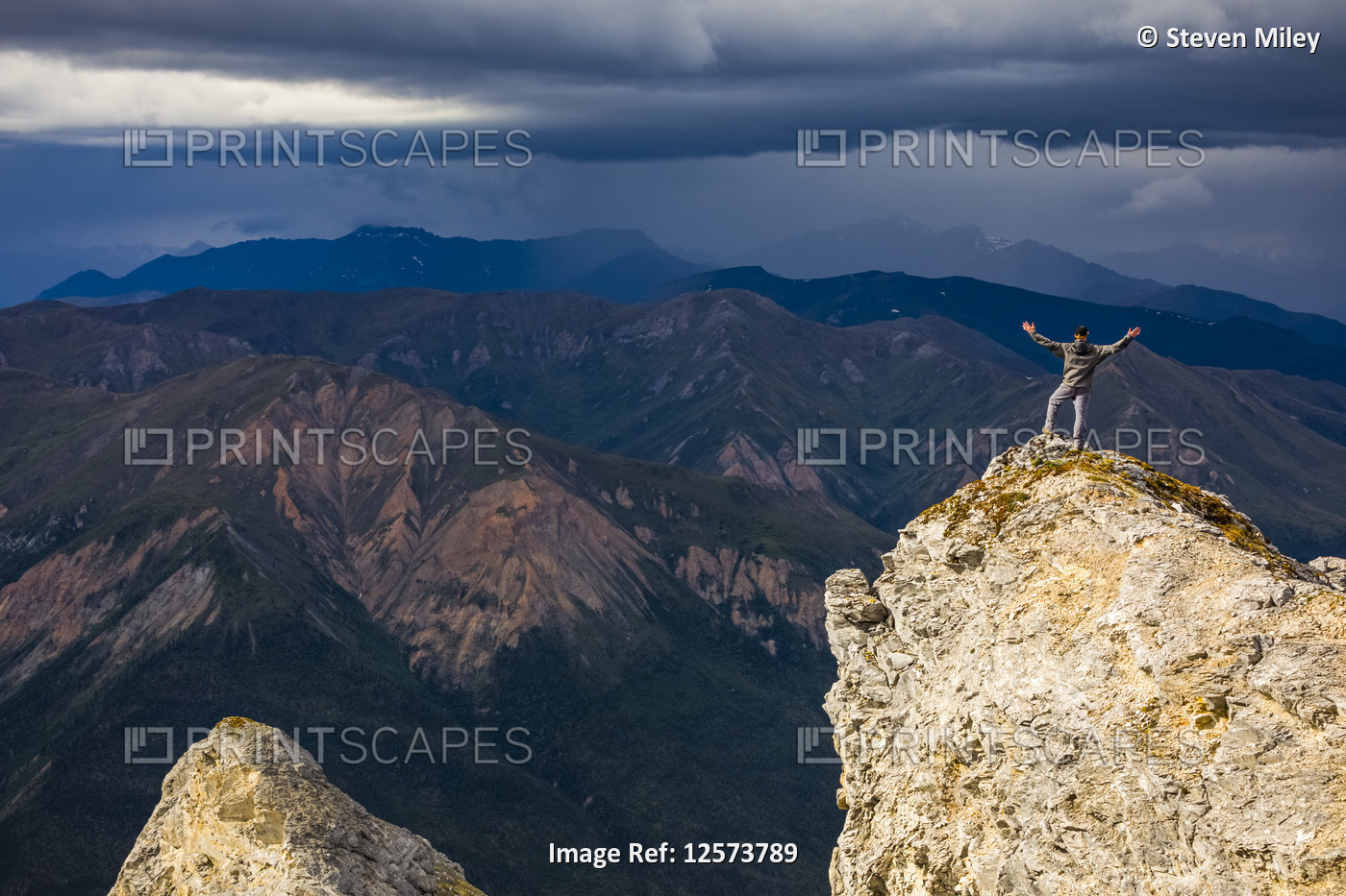 Sunshine illuminates a hiker on top of Sukakpak Mountain as storm clouds brew ...
