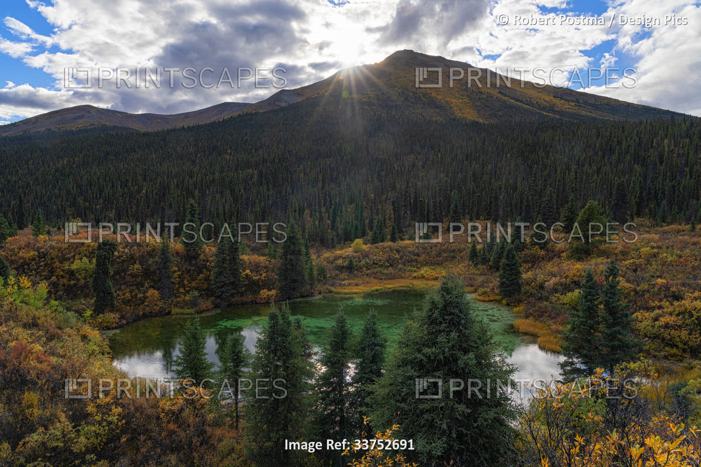 Sunburst over the mountains and reflected in a small pond along the South Canol ...