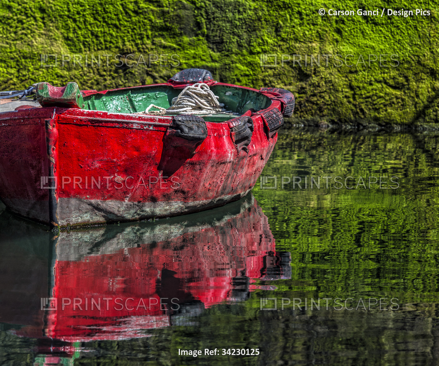 Small, wooden fishing boat moored to the shore with a mirror image reflection ...