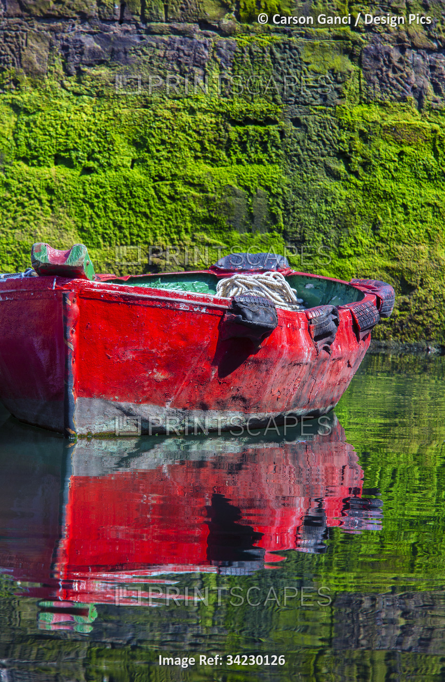 Small, wooden fishing boat moored to the shore with a mirror image reflection ...