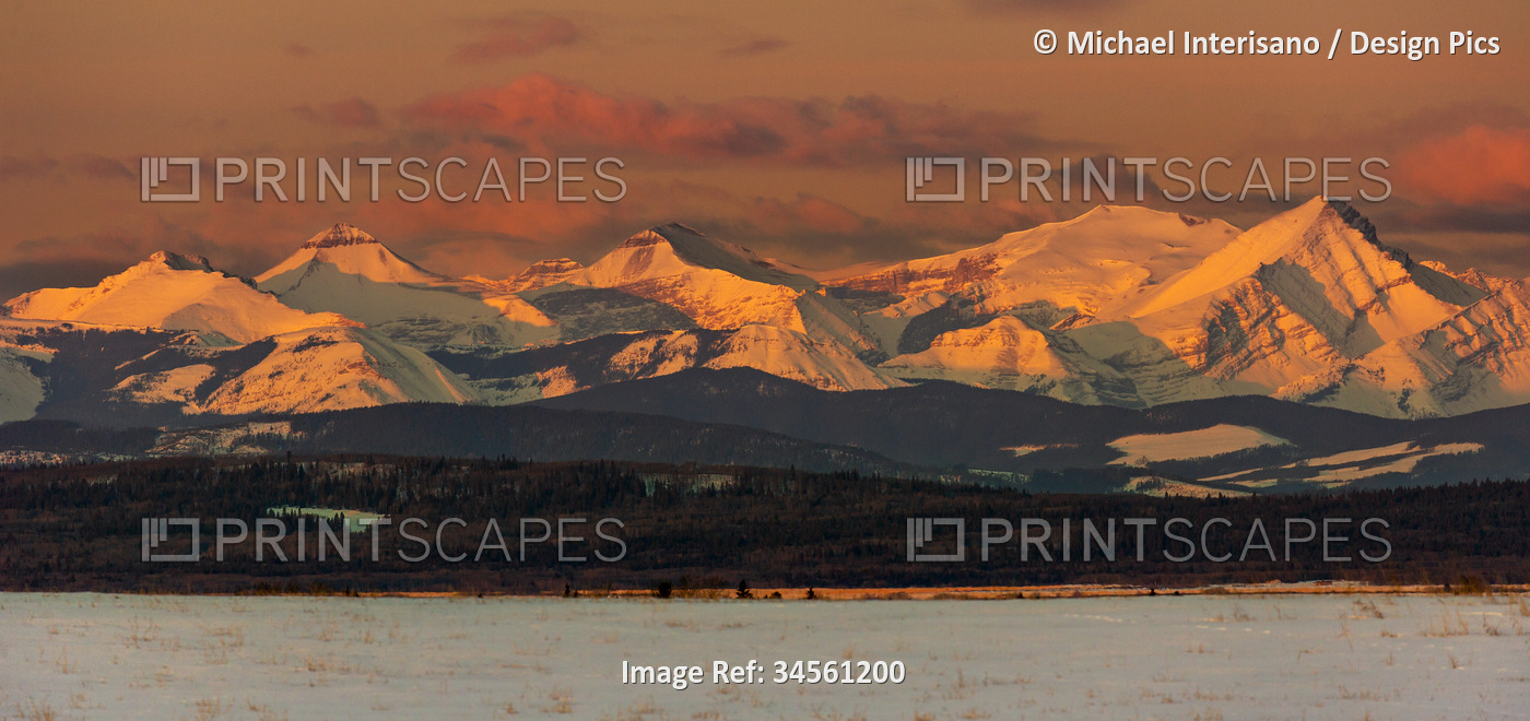 Snow-covered mountain range glowing with the warm light of sunrise and warm ...